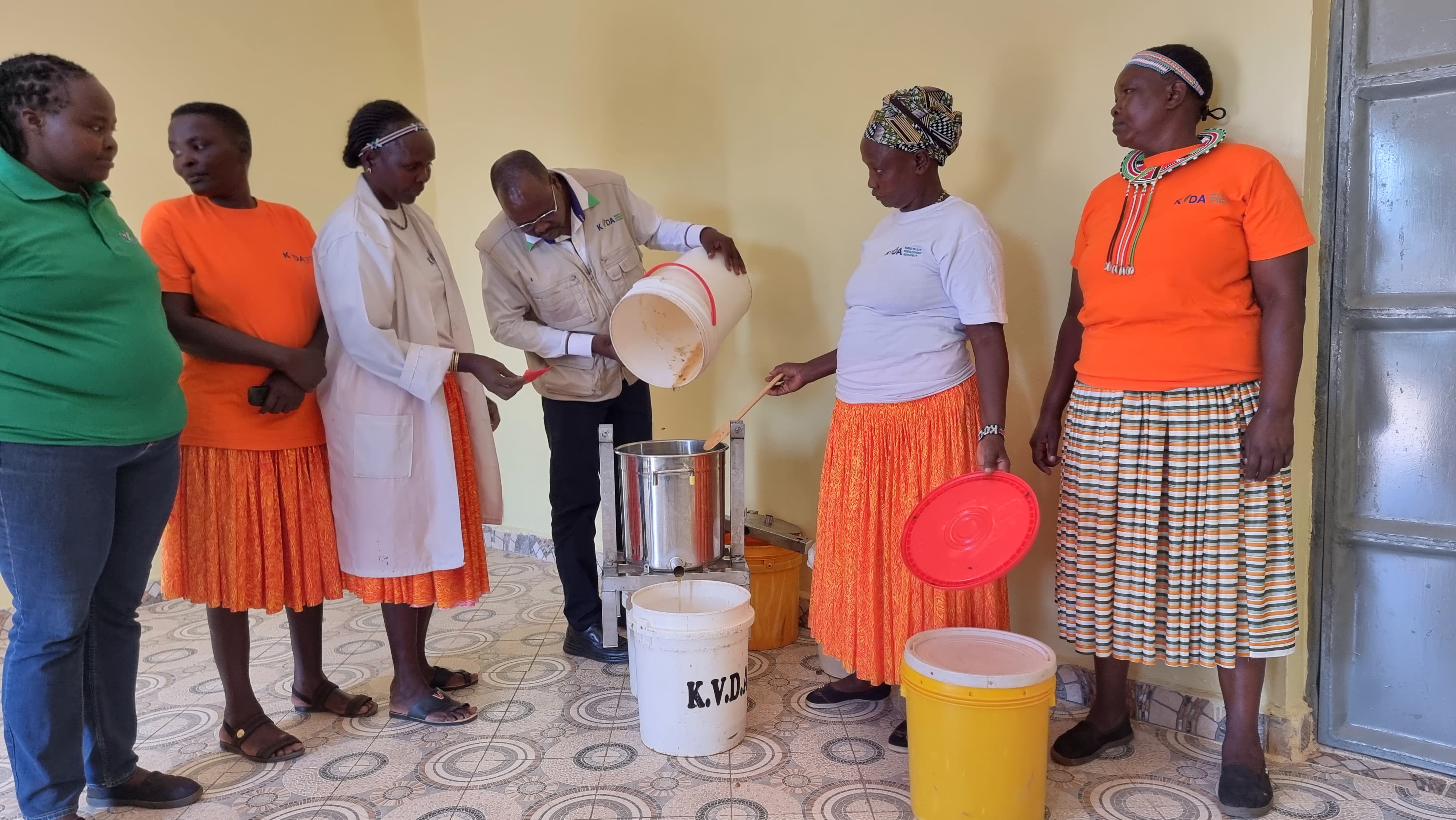 Moses Kipchumba, the Acting Managing Director of Kerio Development Authority, joins members of a women group at the centre during a live demonstration of honey processing. The MD is seen pouring honey from a jerrycan into a honey processing machine, showcasing the extraction and processing of honey from combs and wax. PHOTO: ANTHONY MELLY
