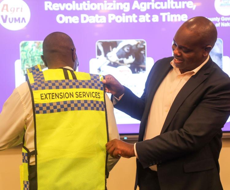 Chief Officer Newton Mwaura (agriculture) assisting an extension officer to wear an identification jacket