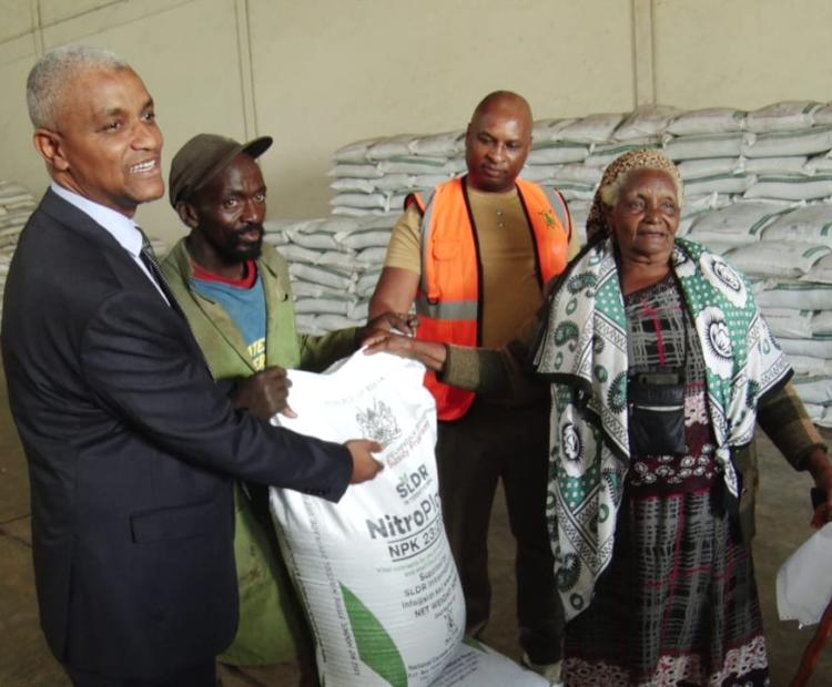 The National Fertilizer Technical Committee Chairman Haron Khator (left) presents a Thika farmer with subsidized fertilizer she had purchased at the National Cereals and Produce Board in Thika town.