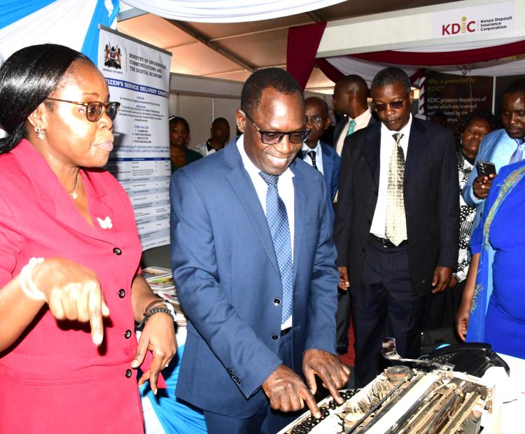 Principal Secretary, State Department for Broadcasting and Telecommunication Stephen Isaboke (2nd left) is being briefed by Officers Rosemary Ngesa (left) Odhiambo Omondi (third left) and Rose Andanje (second right) on the evolution of KNA Tools of Trade at the ICT Ministry’s stand during the 2025 African Public Service Day (APSD) National celebrations at Kenyatta International Convention Center (KICC) Nairobi. PHOTO/NORAH BOCHERE