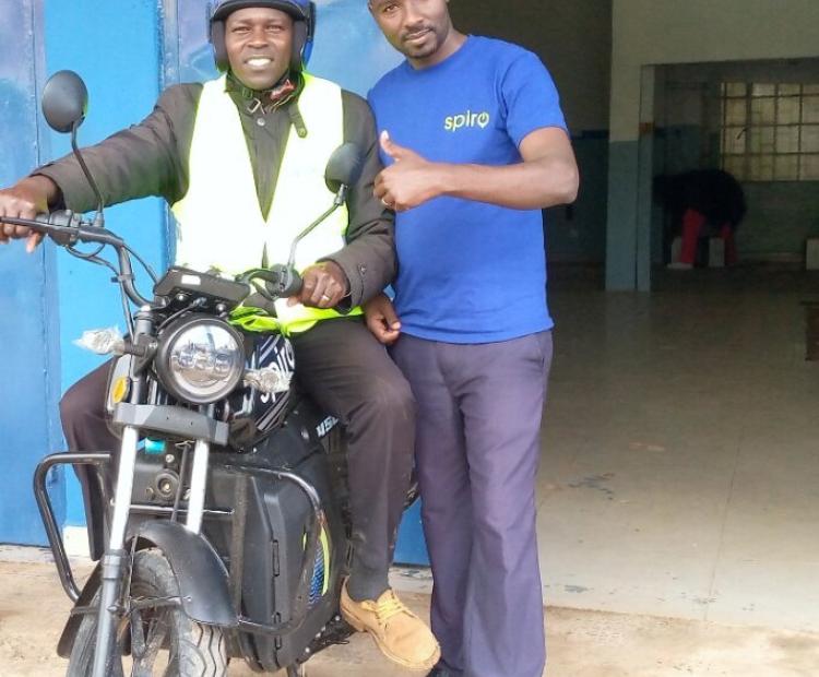 A satisfied boda boda operator Bernard Tonui poses with his newly acquired electric bike at the Spiro Kericho branch. On the right is a sales agent with Spiro Company, Aaron Koech. PHOTO: SARAH NJAGI