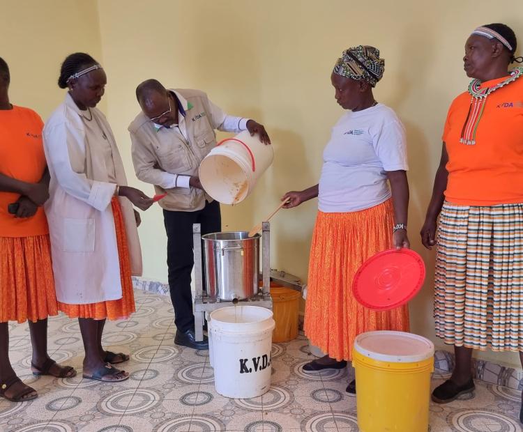 Moses Kipchumba, the Acting Managing Director of Kerio Development Authority, joins members of a women group at the centre during a live demonstration of honey processing. The MD is seen pouring honey from a jerrycan into a honey processing machine, showcasing the extraction and processing of honey from combs and wax. PHOTO: ANTHONY MELLY